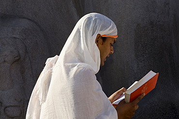 Jain pilgrim is reciting religious texts at the feet of the gigantic statue of Gomateshwara in Sravanabelagola, Karnataka, India, Asia