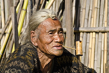 Old Apatani man with the typical hair knot at the forehead, in front of his house, Hong village, Arunachal Pradesh, India, Asia