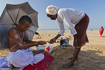 Local priest receiving money after leading a religious ceremony on the beach of Varkala, India, Asia