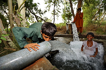 Children cooling off at the catchment of a spring that is fed by water pipes, Basti Lehar Walla village, Punjab, Pakistan, Asia