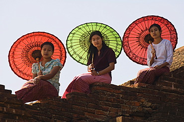 Young Burmese women with coloured parasols sitting on a temple wall, Bagan, Myanmar