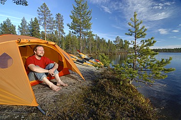 Man sitting in front of a tent at a lakeside, looking into the distance, Femundsmarka National Park, Femundsmark, Norway