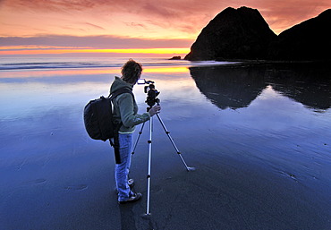 Camerawoman with movie camera filming sunset with a tripod at Meyers Creek Beach, Pistol River State Park, Oregon Coast, Oregon, USA, North America