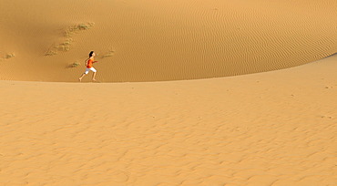 Woman running over sand dunes and structures near Mui Ne, Red Sand Dunes, Vietnam, Asia