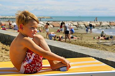 Boy sitting on a lounger on the beach, Caorle, Veneto, Italy