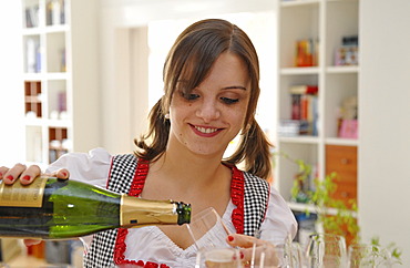 Young woman in dirndl, pouring champgane into a glass