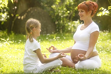 Girl and pregnant woman in yoga position in the garden