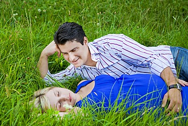 Man lying with his pregnant woman in the grass and looking at her tenderly