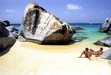 Sunbathing couple, sailboat in the distance, "The Baths, " Virgin Gorda Island, British Virgin Islands, Lesser Antilles, Caribbean