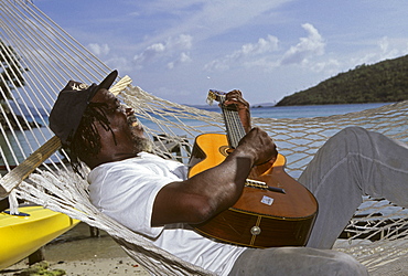 Man laying in a hammock playing the guitar, Jost Van Dyke Island, British Virgin Islands, Lesser Antilles, Caribbean