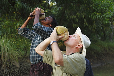 Tourist and an Indian man drinking from a coconut, Kerala, South India, India, Asia