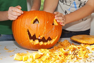 Two girls, about 14 years, carving a face into a Halloween pumpkin