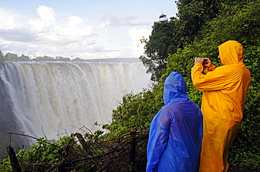 Tourists in rain jackets photographing the Victoria Falls, waterfall on the Zimbabwean side of the river Zambezi, Victoria Falls town, Zimbabwe, Africa