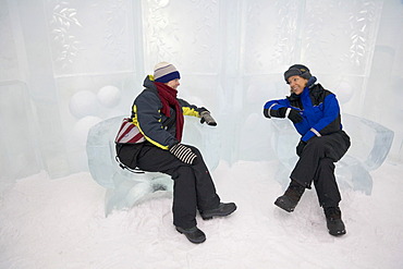 Two women sitting on chairs carved out of ice in the Icehotel in Jukkasjaervi, Lappland, North Sweden, Sweden