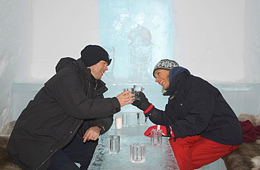 Ice bar of the ice hotel of Jukkasjaervi, woman and man clinking ice glasses, Jukkasjaervi, Lappland, Northern Sweden