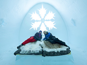 Two tourists lying on a bed in a bedroom in the ice hotel in Jukkasjaervi, Kiruna, Lappland, northern Sweden, Sweden, Europe