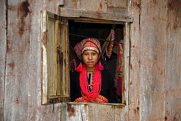 Young woman of the Akha Pala tribe looking out of a window dressed in a colourful head-dress and a red necklace, Ban Saenkham Tai, Phongsali Province, Laos, South East Asia