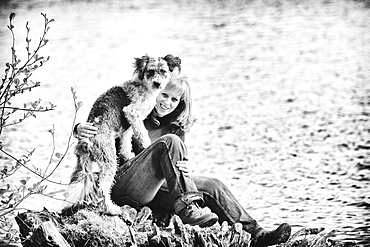 Woman sitting with her dog on a rock by a lake