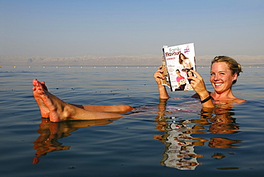 Young woman reads newspaper floating in Dead Sea, Jordan, Asia