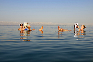 Young couple reads newspaper floating in Dead Sea, Jordan, Asia