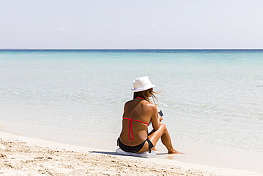 Woman sitting down by the sandy beach, Puglia, Italy, Europe