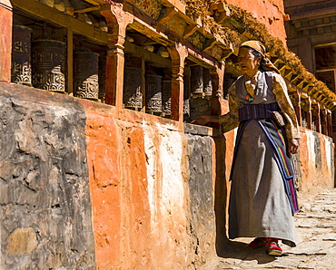 Native woman walking along Mani Wall and spinning prayer wheels, Kagbeni, Mustang District, Nepal, Asia