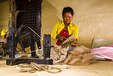 Native woman spinning sheep's wool with traditional spinning wheel in front of house, Ghandruk, Kaski District, Nepal, Asia