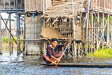 Boy, young man rowing, traditional stilt houses behind, Inle Lake, Nampan, Shan State, Myanmar, Asia