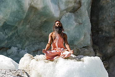 A Sadhu, holy man, is sitting and meditating in lotus pose, padmasana, on a block of ice at Gaumukh, the main source of the holy river Ganges, Gangotri, Uttarakhand, India, Asia