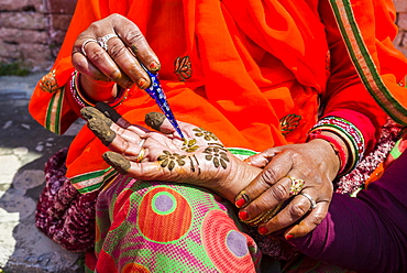 An indian woman is painting a hand with henna, in front of Badrinath Temple, one of the Dschar Dham destinations, Badrinath, Uttarakhand, India, Asia