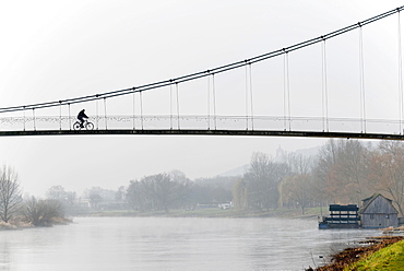 Cyclist crossing a suspension bridge, water mill on the Weser river, Minden, North Rhine-Westphalia, Germany, Europe