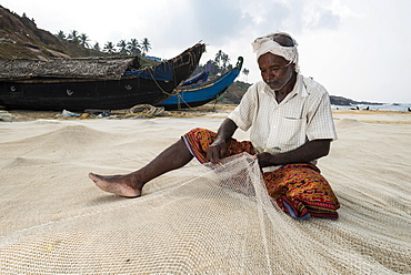 Fisherman repairing fishing nets on the beach, Vizhinjam, Kerala, India, Asia