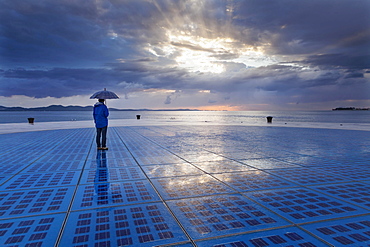 Woman holding an umbrella, standing on the solar art installation ""Greeting to the Sun"", Zadar, Dalmatia, Croatia, Europe