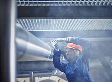 Technician, mechanic with orange helmet mounting a refrigeration line bracket, Austria, Europe