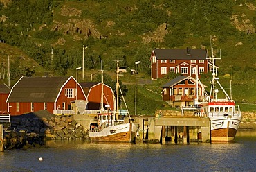 Typical red Rorbuer huts, rorbu, and boats illuminated by warm evening light near Straume on the island of Langoya, Langoya, part of the VesterÃ‚len, Vesteralen archipelago, Nordland, Norway, Europe