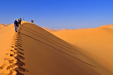 Group of tourists hiking through the sand dunes of Erg Mehejibad, Ahnet, Algeria, Sahara, North Africa