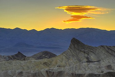 Emerging Sierra Wave cloud form in the evening light, view from Zabriskie Point to Manly Beacon with eroded rocks discoloured by minerals, Panamint Range at back, sunrise, Death Valley National Park, Mojave Desert, California, United States of America