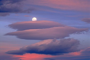 The rising moon behind colorful evening clouds near Lake Wanaka, South Island, New Zealand