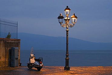 A Motorino scooter beside a street lamp at the shore of Lake Garda at the blue hour in Gargnano, Lombardia, Italy, Europe