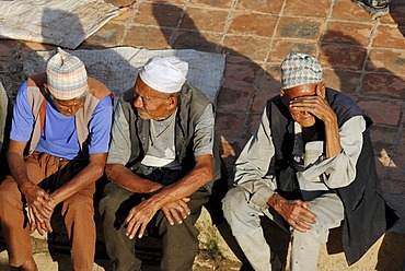 Men sitting on the Taumadhi Square, with traditional headwear, Bhaktapur, Kathmandu Valley, Nepal, Asia