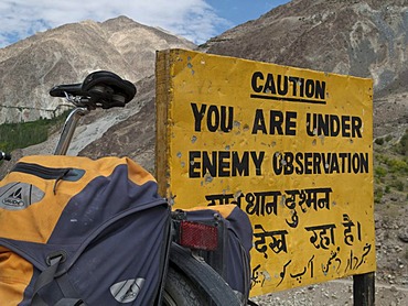 Traveller's bicycle leaning against warning sign, "Caution, you are under enemy observation", in the area around Kargil, Jammu and Kashmir, India, Asia