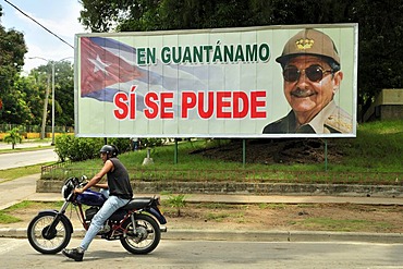 Motorcyclist in front of a sign with revolutionary propaganda, En Guantanamo si se puede, Guantanamo, Cuba, Caribbean