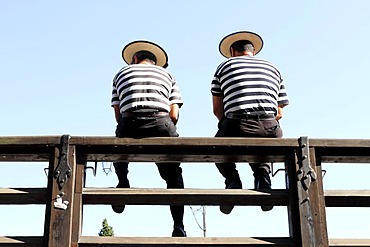 Two gondoliers sitting on a railing, from behind, Venice, Italy, Europe