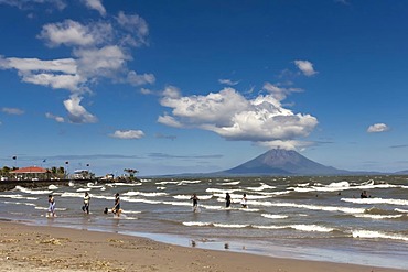 People walking on the shallow shore of Lago de Nicaragua with the volcanic island of Ometepe and the stratovolcano Volcan Concepcion at back, San Jorge, Nicaragua, Central America