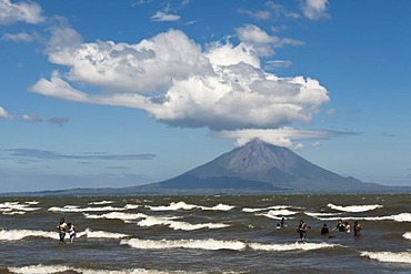 People walking on the shallow shore of Lago de Nicaragua, volcanic island of Ometepe and the stratovolcano Volcan Concepion at back, San Jorge, Nicaragua, Central America