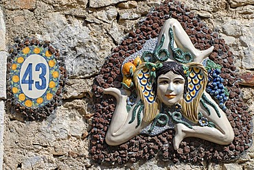 The symbol of Sicily, a girl's head surrounded by snakes and small wings with three running angled legs, sun wheel, on a wall, Taormina, Messina, Sicily, Italy, Europe