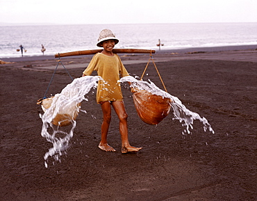 Young boy throwing sea water onto sand to make salt, Bali, Indonesia, Southeast Asia, Asia