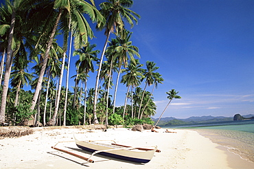 Couple sunbathing on beach with outrigger boat in foreground, El Nido, Bascuit Bay, Palawan, Philippines, Southeast Asia, Asia