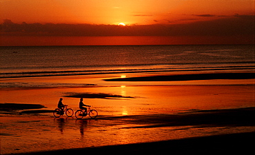 Couple cycling on beach at sunset