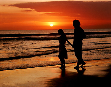 Sunset over sea and silhouette of couple walking on beach